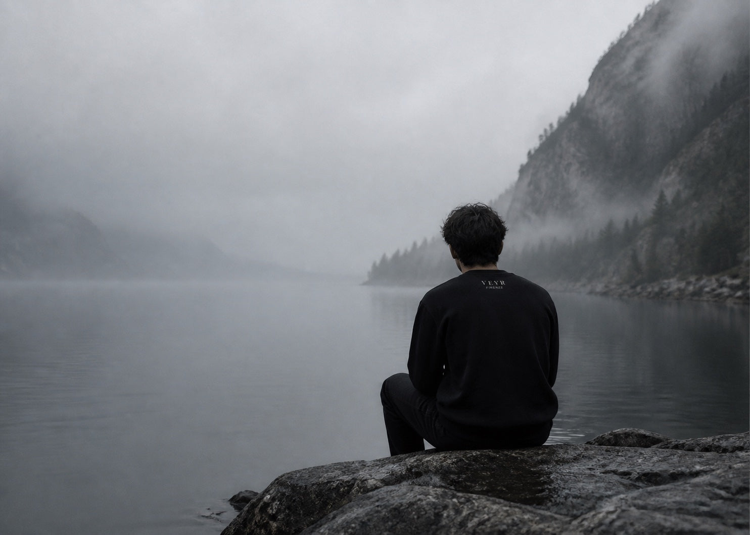 A person in a black VEYR crew sitting beside still water