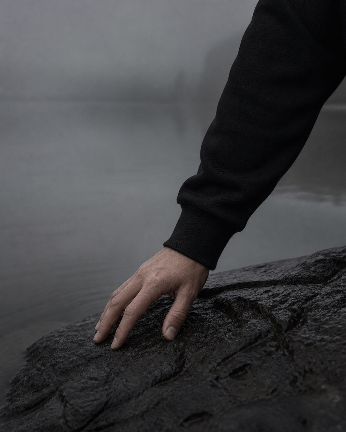 A hand in a black VEYR sleeve resting on wet stone